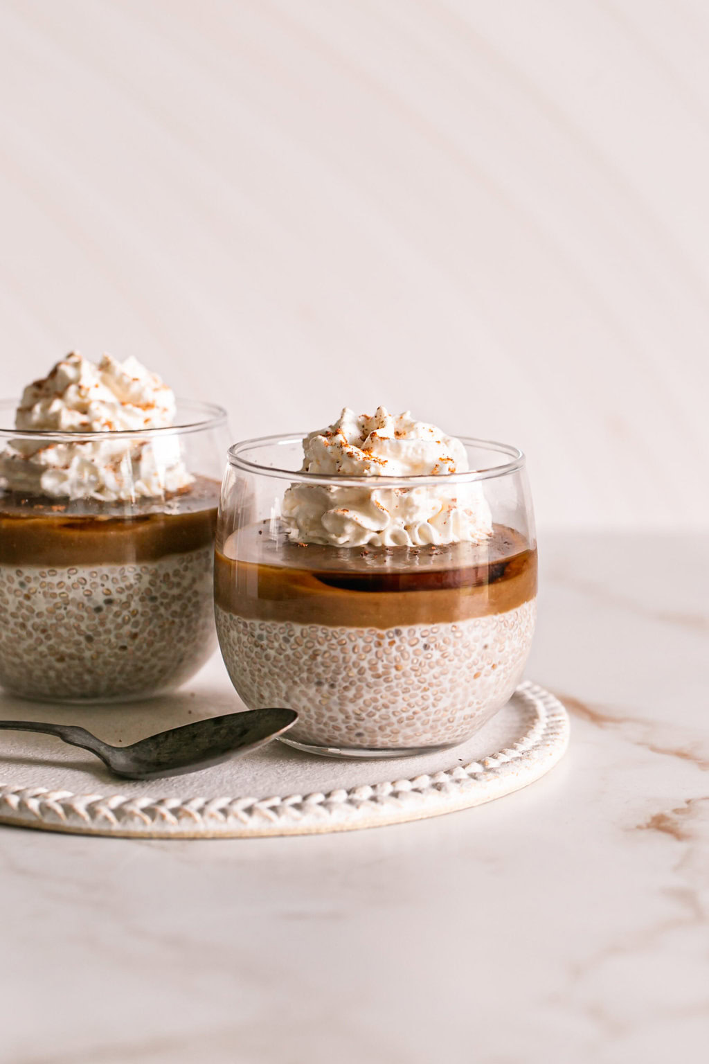 two glasses of caramel eggnog chia pudding topped with vegan caramel, maple syrup and whipped cream