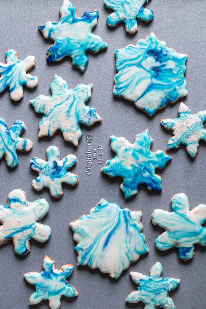 a close up of blue and white decoratedgrain-free marbled snowflake sugar cookies on a Calphalon baking sheet
