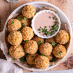 a bowl full of mashed potato croquettes with a bowl of paprika dipping sauce garnished with fresh chives and parsley