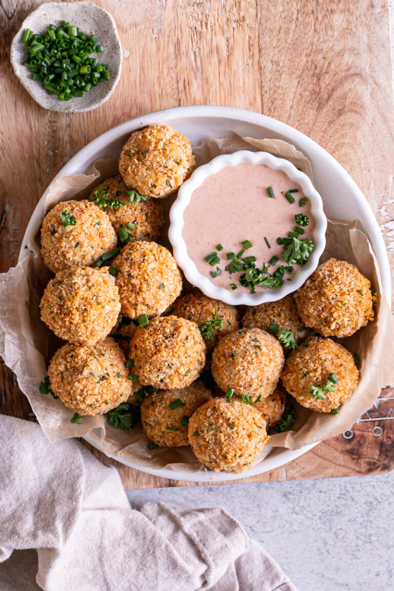 a bowl full of mashed potato croquettes with a bowl of paprika dipping sauce garnished with fresh chives and parsley