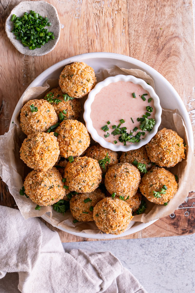 a bowl full of mashed potato croquettes with a bowl of paprika dipping sauce garnished with fresh chives and parsley