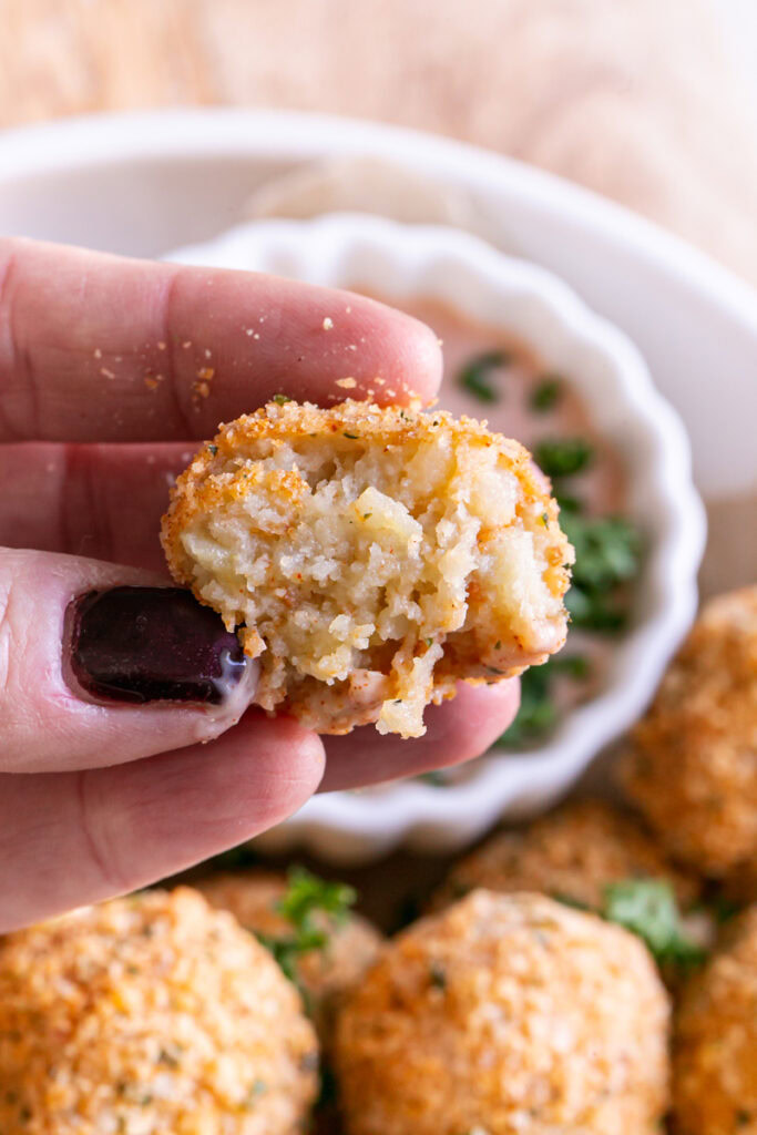 close up shot of hands holding a bitten mashed potato croquette to reveal the potato inside