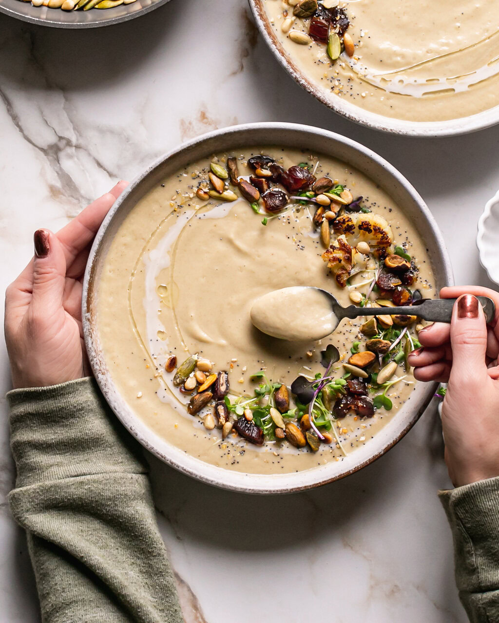 hands around a bowl of roasted cauliflower soup spooning some out