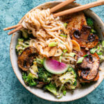 a close up shot of one of the bowls of ramen noodles with noodles wrapped around wooden chopsticks