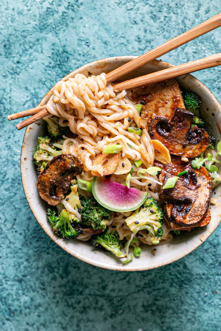 a close up shot of one of the bowls of ramen noodles with noodles wrapped around wooden chopsticks