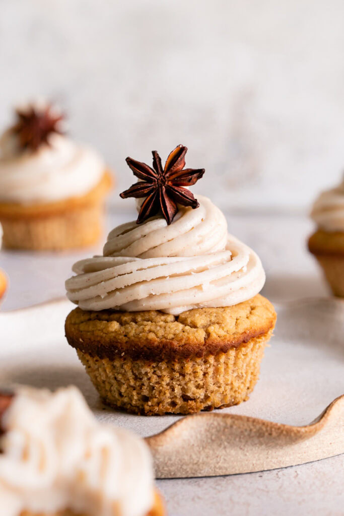 a single frosted chai cupcake on a plate with other cupcakes blurred around it
