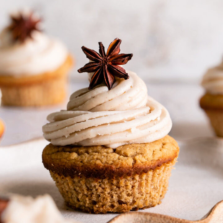 a single frosted chai cupcake on a plate with other cupcakes blurred around it