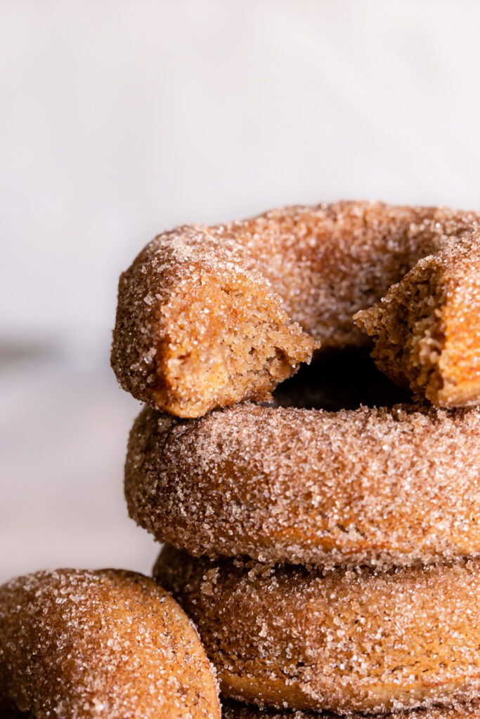 a close up of grain free cinnamon sugar donuts stacked on top of one another with the top one with a bite out of it