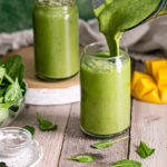 action shot of pouring Anti-Inflammatory Vegan Green Smoothie into one of the glasses with another full smoothie in a glass behind it