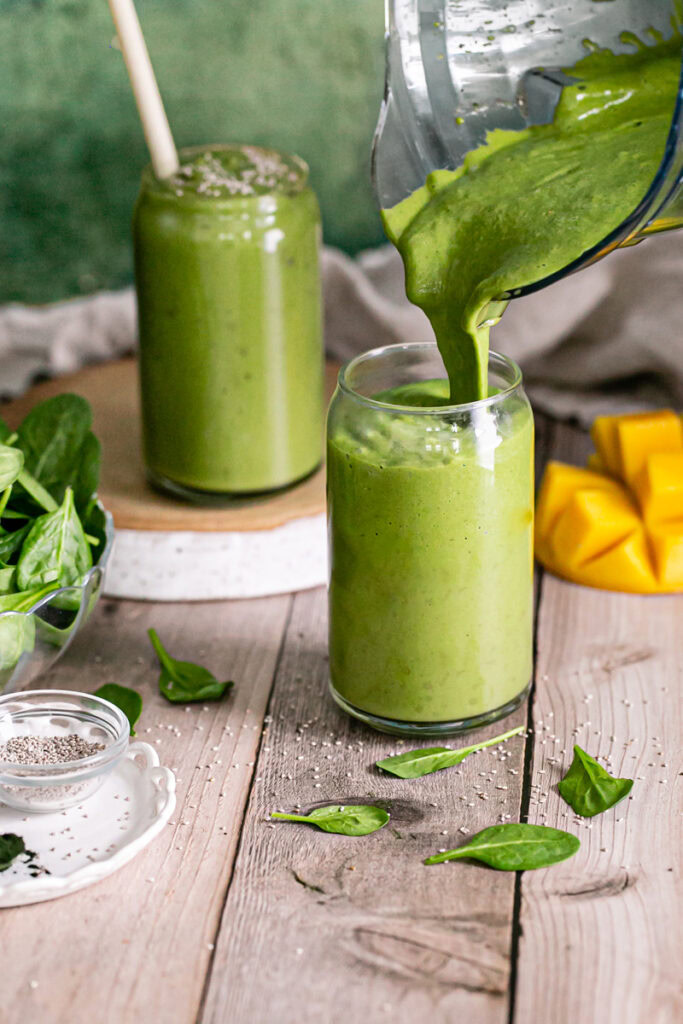 action shot of pouring Anti-Inflammatory Vegan Green Smoothie into one of the glasses with another full smoothie in a glass behind it