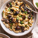 a bowl of Creamy Alfredo Style Mushroom Pasta with another bowl peeking in on the lower left corner with a linen napkin in the lower right