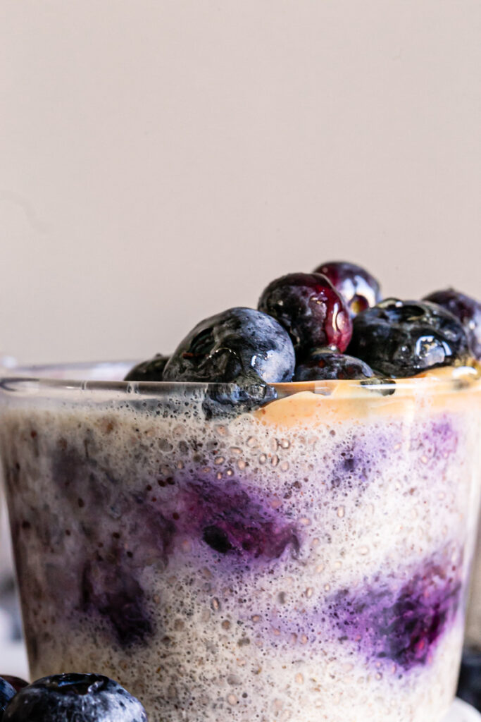 a close up of a glass of Blueberry Overnight Quinoa topped with peanut butter and fresh blueberries