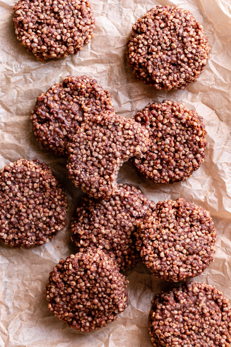 Crispy Quinoa Cacao Cookies piled on a piece of parchment paper, one with a bite taken out of it