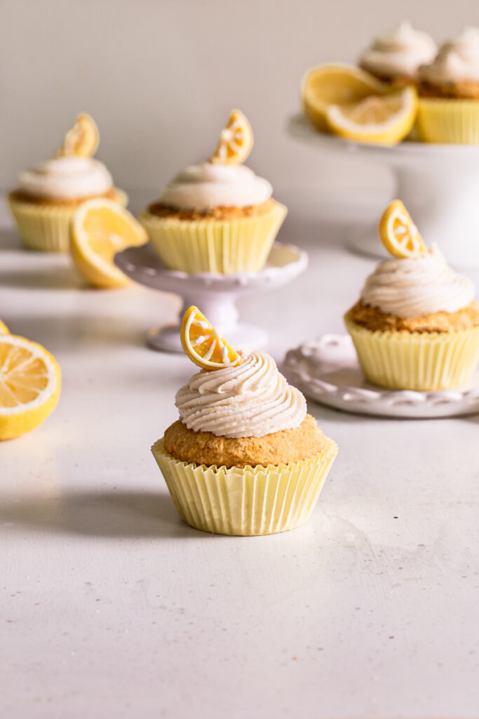 grain-free lemon cupcakes with vanilla frosting decorated with a lemon candy wedge and fresh lemons around them