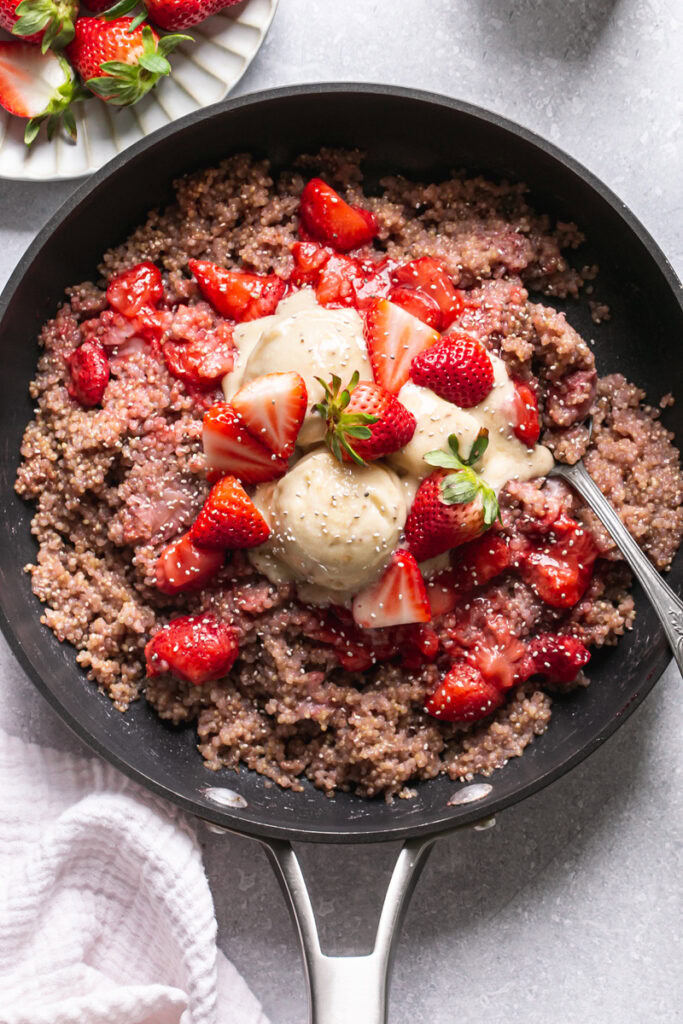 a skillet of strawberries and cream breakfast quinoa topped with fresh strawberries and banana nice cream sprinkled with chia seeds