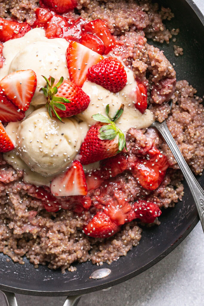 a close up of a skillet of strawberries and cream breakfast quinoa topped with fresh strawberries and banana nice cream sprinkled with chia seeds and a spoon in it