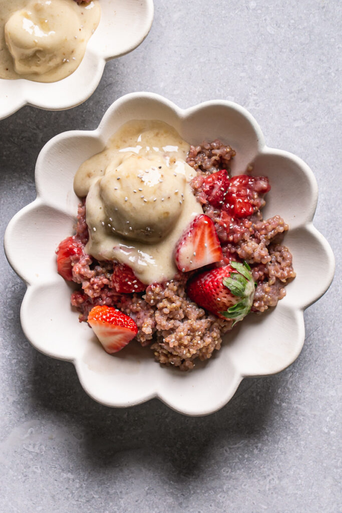 a close up of a bowl of strawberries and cream breakfast quinoa with a scoop of banana nice cream