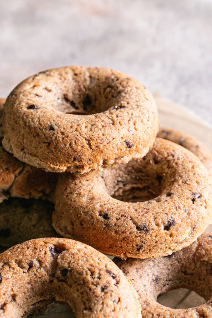 vertical image of grain-free banana bread donuts piled on a round wire cooling rack