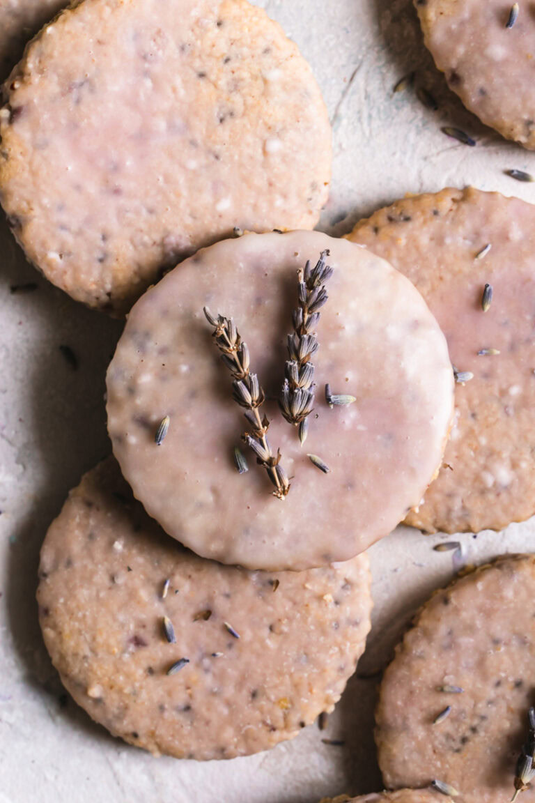 Lavender Vanilla Oatmeal Shortbread Cookies piled on top of one another iced with a light purple icing, the top cookie with lavender sprigs on top