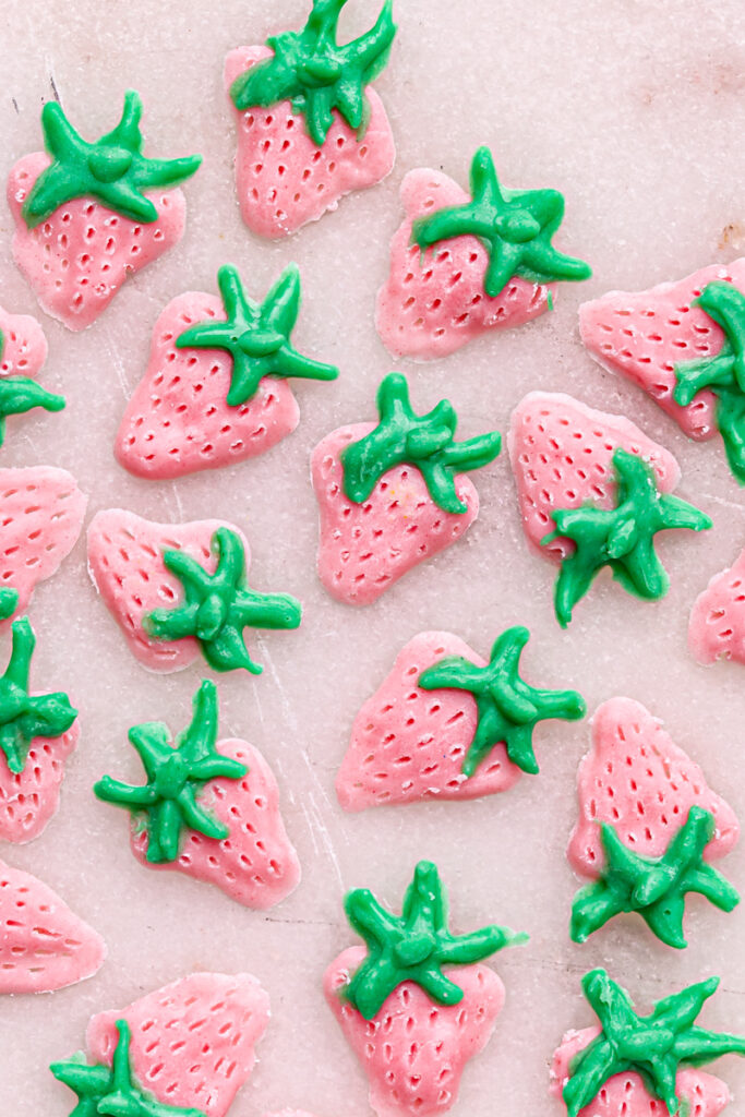 cute little pink strawberries pained with white chocolate onto a piece of wax paper.