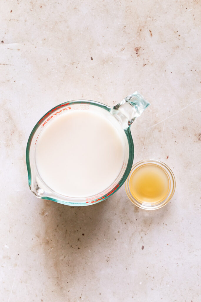 a glass measuring cup filled with flax milk and a small bowl of apple cider vinegar next to it