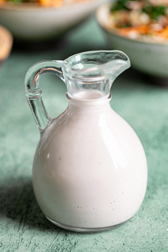 bottle of the creamy tahini dressing with the quinoa bowls blurred in the background