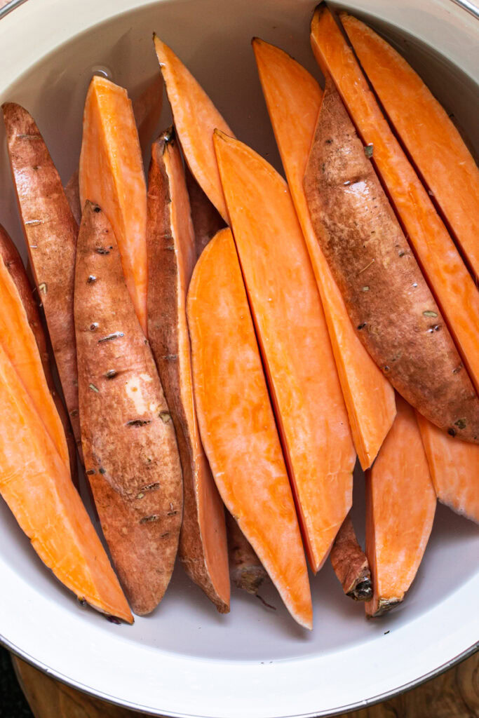 sliced sweet potato wedges soaking in a bowl of cold water