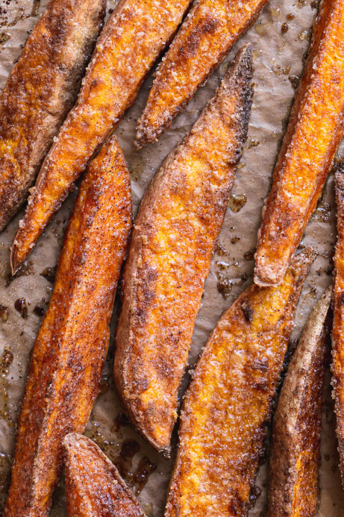 crispy roasted cinnamon sugar sweet potato wedges on a parchment lined baking sheet right from the oven