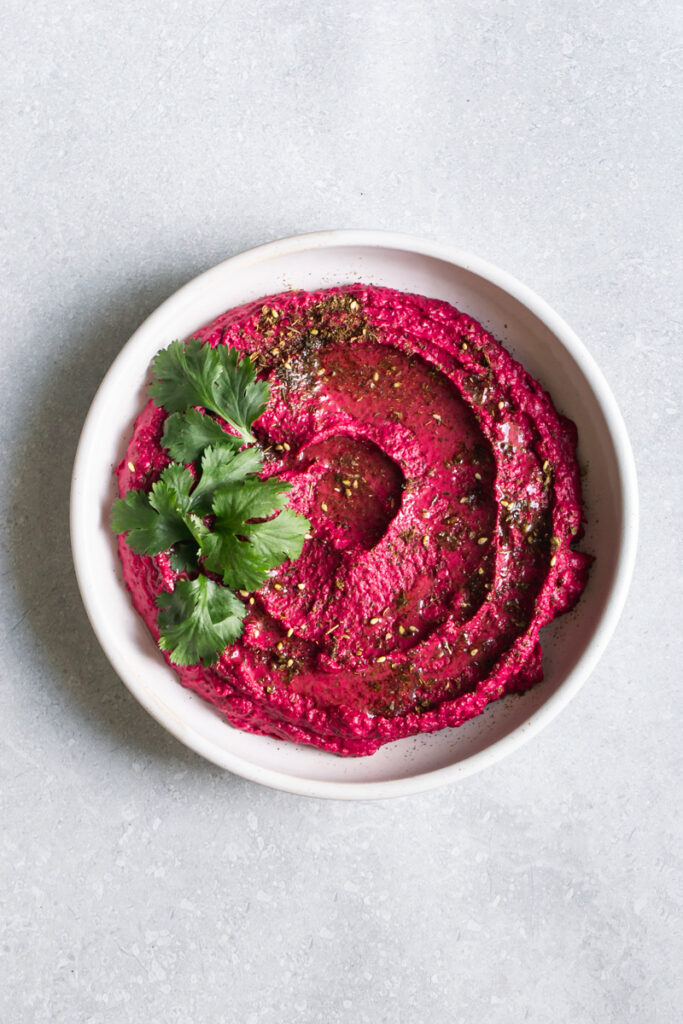 a bowl of Za'atar Roasted Beet White Bean Hummus garnished with fresh cilantro leaves