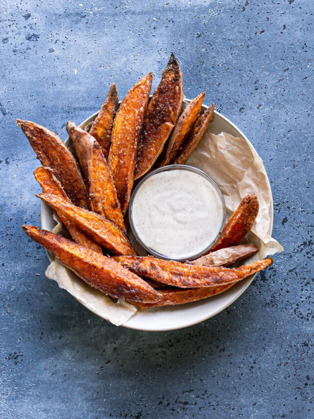 crispy cinnamon sugar sweet potato wedges in a parchment lined bowl surrounding a bowl of coconut sugar sour cream dipping sauce