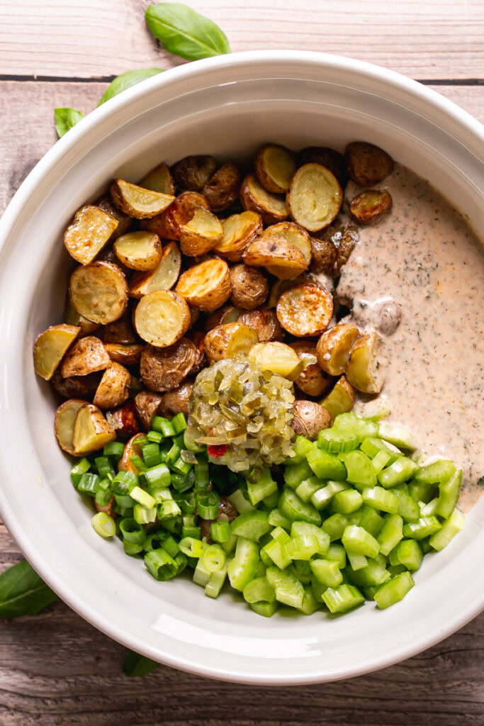 a bowl of all the potato salad ingredients before mixing it all together. Roasted potatoes, chopped celery and green onion, sweet relish and the garlic herb dressing