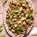 an oval platter with roasted potato salad on it garnished with fresh basil leaves on a wooden table