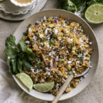 a bowl of Dairy-Free Mexican Street Corn Quinoa Salad with a plate of fresh cilantro leaves and a half of lime above it and a bowl of dressing on the other side.