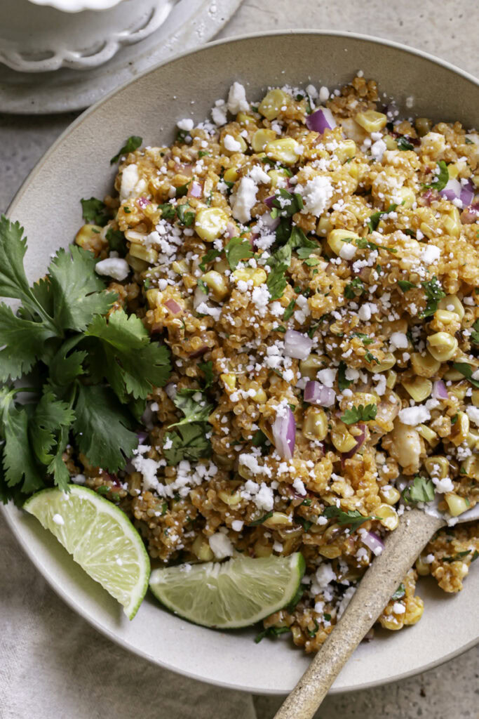 a close up of a bowl of Dairy-Free Mexican Street Corn Quinoa Salad with a spoon in the bowl.