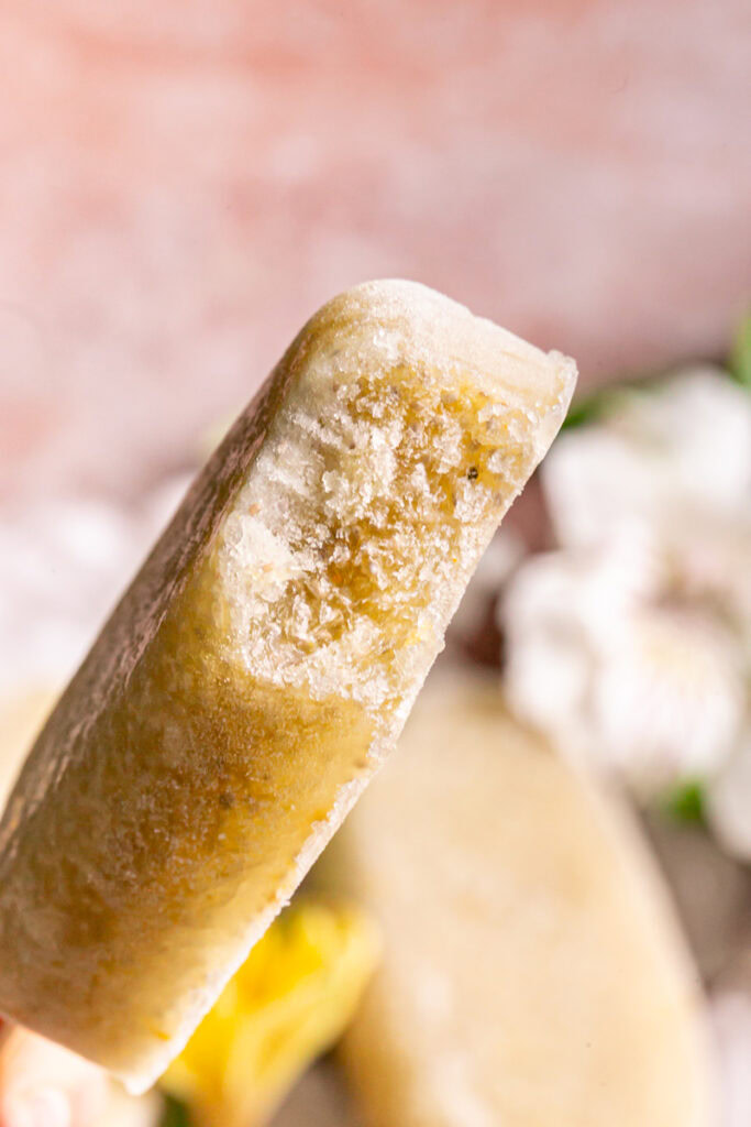 a single Pineapple Coconut Chia Popsicle held up close with a bite taken out of it