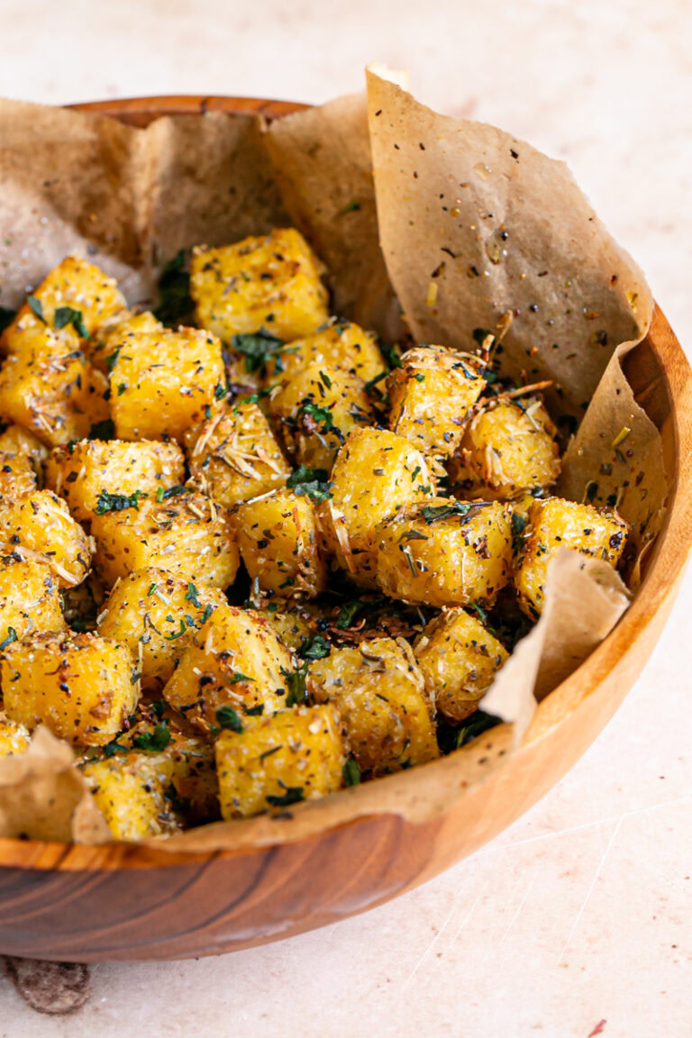 3/4 close up of polenta croutons in a wooden bowl lined with parchment paper