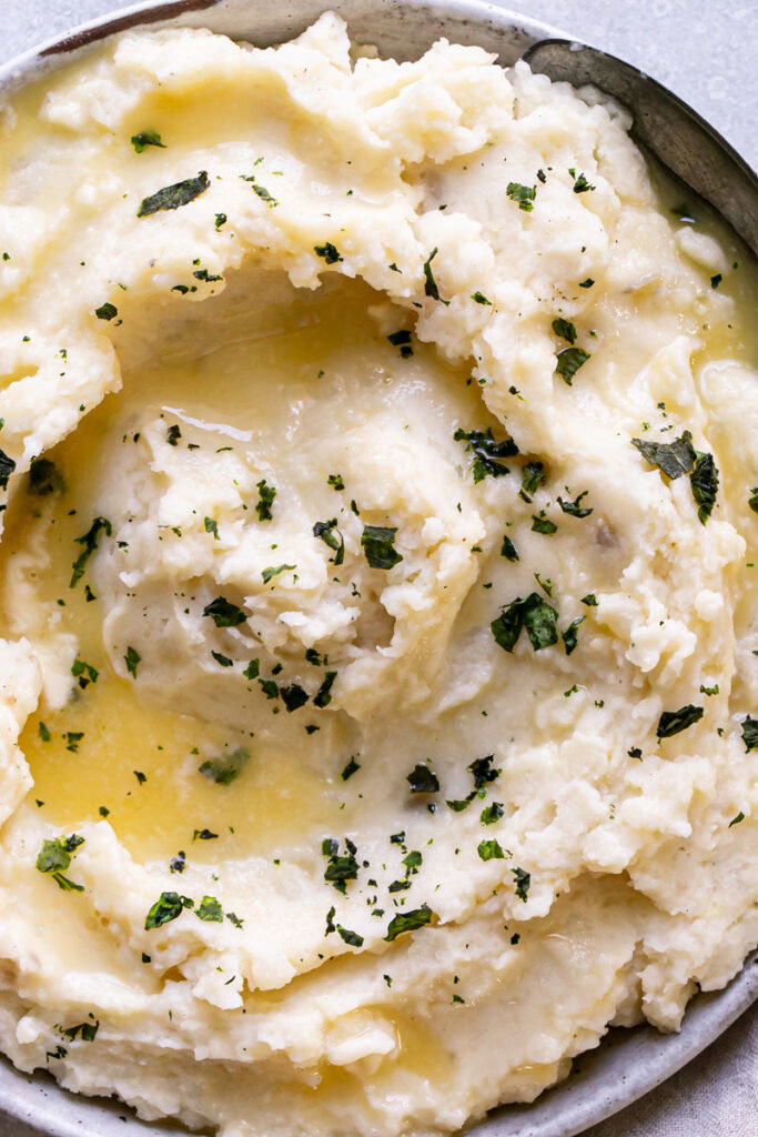 close up of a bowl of Dairy-Free Mashed Potatoes with melted dairy-free butter and garnished with chopped parsley