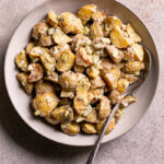 a bowl of roasted caesar potato salad with a spoon in it