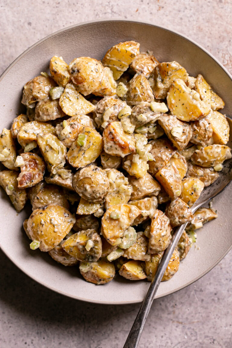 close up of a bowl of roasted caesar potato salad with a spoon in it