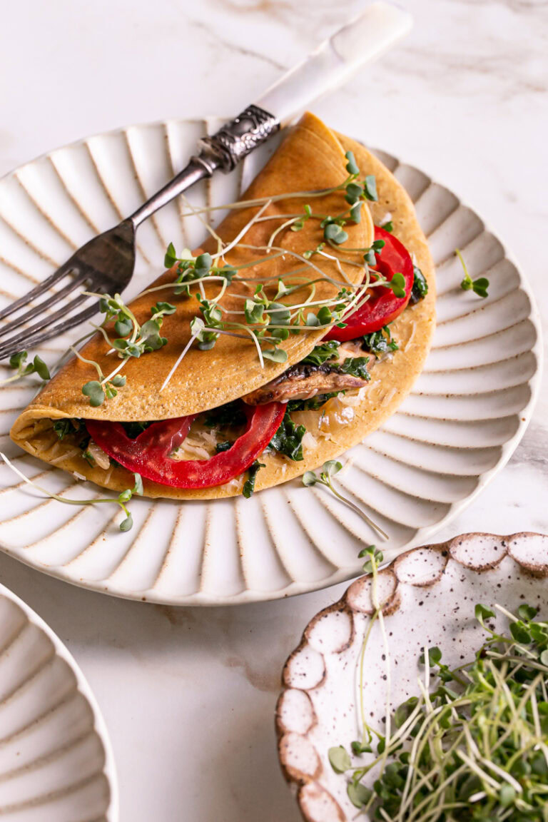 Vegan Gluten-Free Savory Pancake filled with vegan cheese, mushroom, kale and onion, and tomato on a plate garnished with fresh microgreens