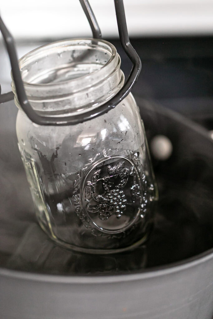 empty canning jars being lowered into a pot of simmering water