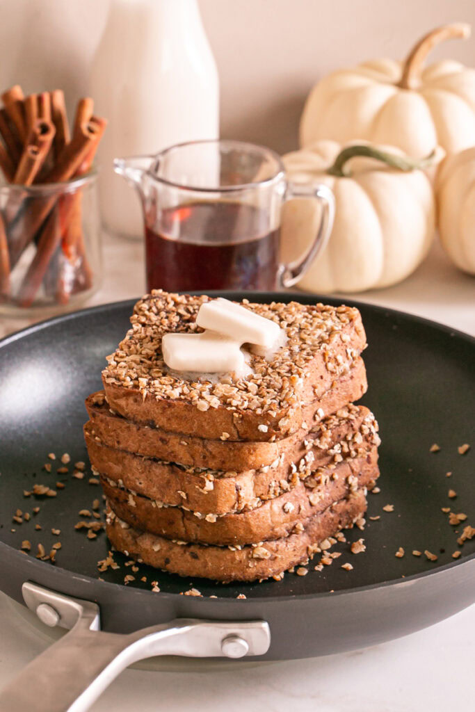pumpkin spice oat crusted French toast stacked in a skillet with two squares of butter on the top one