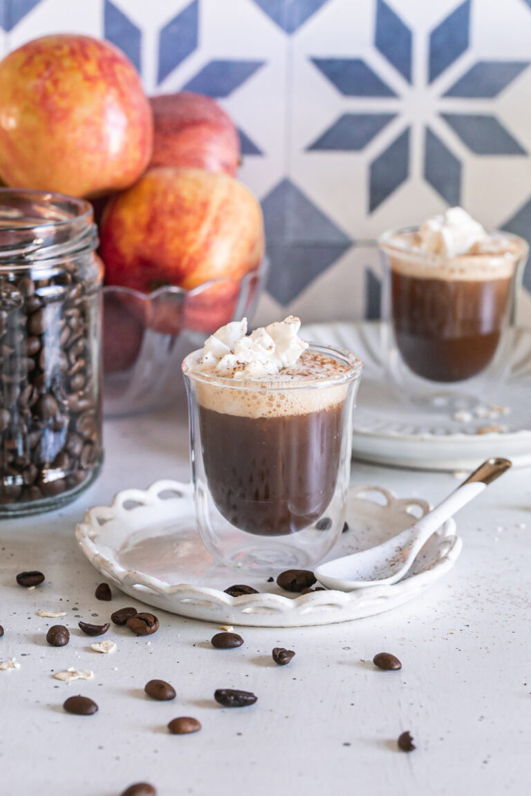Apple Crisp Oatmilk Macchiato with apples and a jar of coffee beans in the background