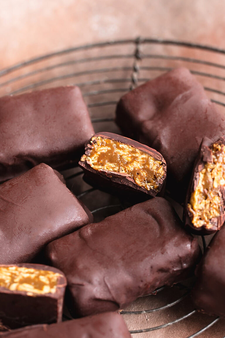 Vegan Butterfinger Bars on a round wire cooling rack, some of them cut open to reveal the inside