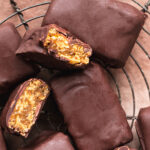 close up of flatly image of Vegan Butterfinger Bars on a round wire cooling rack, some of the bars sliced in half to reveal the filling