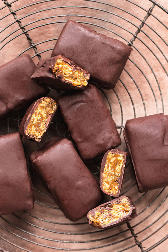 flatly image of Vegan Butterfinger Bars on a round wire cooling rack, some of the bars sliced in half to reveal the filling