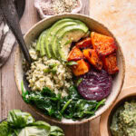 butternut squash pesto buddha bowl with a spoon in it, a small bowl of pesto below it and a glass of fresh basil