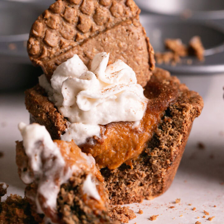 pumpkin pie cookie cup topped with dairy-free whipped cream and an acorn cookie, cut open with a fork to see the pumpkin pie filling