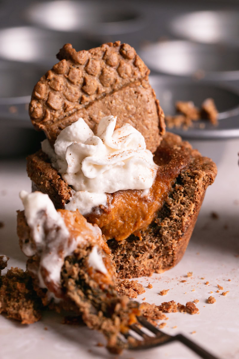 pumpkin pie cookie cup topped with dairy-free whipped cream and an acorn cookie, cut open with a fork to see the pumpkin pie filling