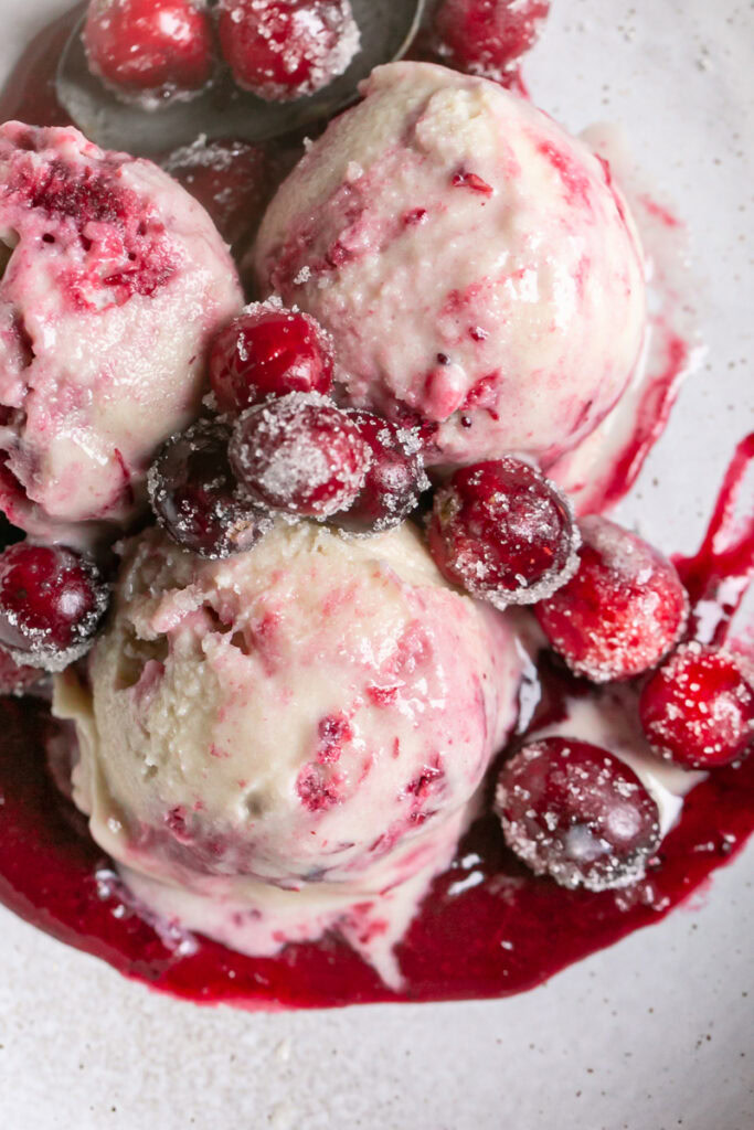 a close up of three scoops of homemade dairy free cranberry swirl ice cream in a bowl topped with sugared cranberries